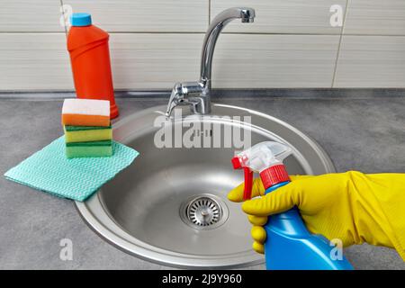 Hände in gelben Gummihandschuhen halten eine Sprühflasche mit Reinigungsmittel Stockfoto