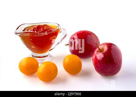 Rote Kirschpflaumenäpfel und Obstkonfitüre in einem Glas-Soße-Boot isoliert auf weißem Hintergrund Stockfoto