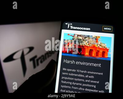Person, die Mobiltelefon mit der Webseite der Offshore-Bohrgesellschaft Transocean Ltd. Auf dem Bildschirm vor dem Logo hält. Konzentrieren Sie sich auf die Mitte des Telefondisplays. Stockfoto