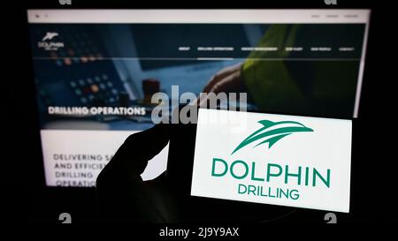 Person, die das Smartphone mit dem Logo der Firma Dolphin Drilling Holdings Limited auf dem Bildschirm vor der Website hält. Konzentrieren Sie sich auf die Telefonanzeige. Stockfoto