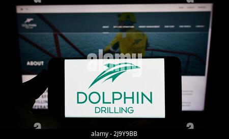 Person mit Mobiltelefon und Logo der Firma Dolphin Drilling Holdings Limited auf dem Bildschirm vor der Business-Webseite. Konzentrieren Sie sich auf die Telefonanzeige. Stockfoto