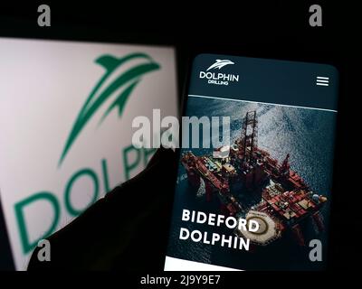 Person, die Mobiltelefon mit der Webseite der Firma Dolphin Drilling Holdings Limited auf dem Bildschirm vor dem Logo hält. Konzentrieren Sie sich auf die Mitte des Telefondisplays. Stockfoto