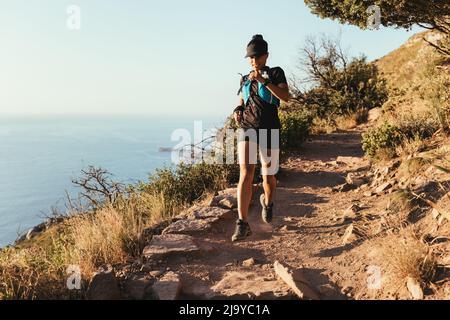 Fit Frau läuft auf dem Bergpfad. Athletinnen in Sportbekleidung üben Langlauf. Stockfoto