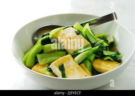 Gesundes, selbstgemachtes vegetarisches Essen, gebratener Bok Choy mit gebratenem weichen Tofu und Austernsauce in einer weißen Schüssel auf einem Marmortisch. Bok Choy, Pak Choi, OR Stockfoto