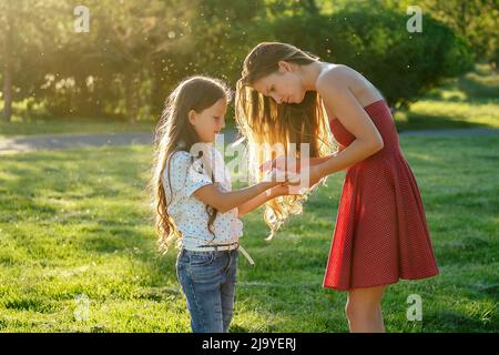 Fürsorgliche und schöne langhaarige Mutter in Cocktail-roten Kleid wischt ihre Tochter die Hände mit nassen Servietten im Park im Sommer . antibakteriell Stockfoto