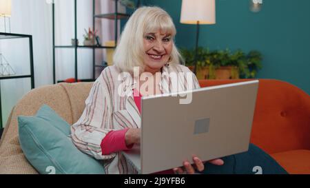 Ältere alte Großeltern beginnen mit der Arbeit an einem Laptop, senden Nachrichten, tätigen Online-Einkäufe zu Hause Stockfoto