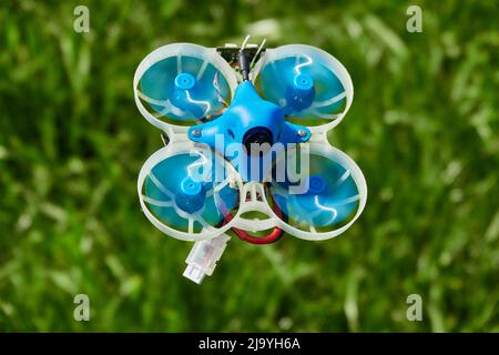 Kleine Drohne blau auch Rennen Quad, mit Schutzgondel in weiß mit einem verschwommenen Hintergrund von Grün. Deutschland. Stockfoto