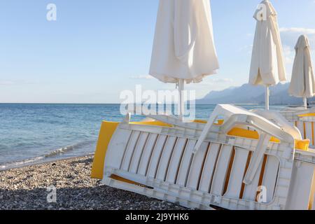 Leerer Strand am Badeort mit gestapelten Sonnenliegen und Sonnenschirmen Stockfoto