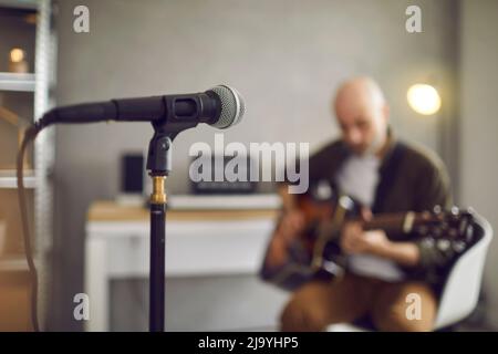 Nahaufnahme des Mikrofons im Aufnahmestudio, im Hintergrund spielt der Musiker Gitarre Stockfoto