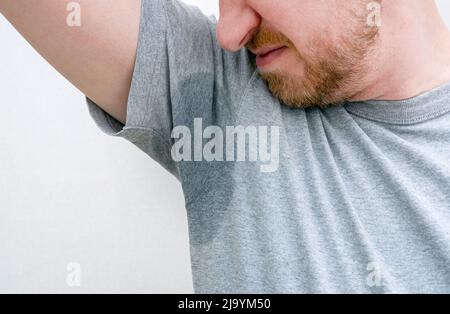 Person schnüffelt Achselhöhlen. Verschwitzte Achselhöhlen, nasser Achselhöhlen, Schweißfleck auf grauem T-Shirt Stockfoto