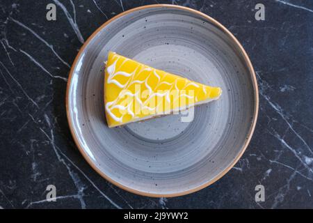 Eine Scheibe köstlicher Zitronenkäsekuchen auf dem Teller mit Marmorhintergrund. Ein Stück Käsekuchen von oben. Stockfoto