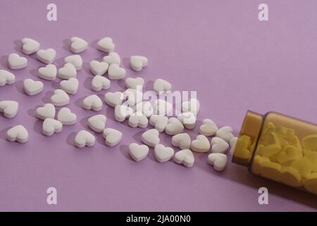 Draufsicht auf verschüttete herzförmige Pillen auf violettem Hintergrund Stockfoto