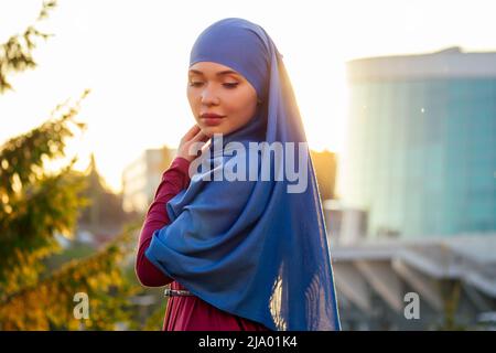 Portrait der schönen muslimischen Frau mit grünen Augen tragen blauen Schal Gesicht geschlossen mit aveil Hintergrund Wald Bäume im Park Sonnenstrahlen bedeckt Stockfoto