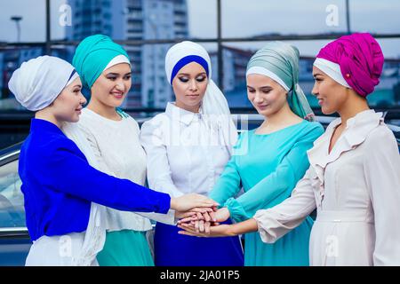 Eine Gruppe von fünf jungen und attraktiven Geschäftsfrauen in muslimischer Kleidung, mehrfarbiger Hijab und ein Turban, der den Kopf bedeckt und die Daumen hochstapelt Stockfoto