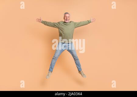 In voller Länge Foto von beeindruckt älteren grauen Frisur Mann springen tragen Pullover Jeans Schuhe auf beigem Hintergrund isoliert Stockfoto