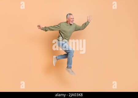 Foto in voller Größe von kühlen älteren grauen Frisur Mann laufen tragen Pullover Jeans Schuhe isoliert auf beigem Hintergrund Stockfoto