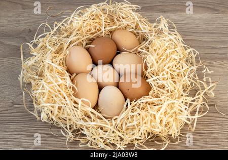 Eine große Anzahl von Eiern. Hühnereier in einem Nest aus Stroh. Isoliert auf Holzhintergrund. Stockfoto