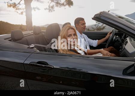 Nahaufnahme einer fröhlichen jungen lächelnden Frau, die im Auto sitzt und einen hübschen Mann fährt Stockfoto