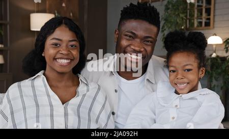 Glückliches afrikanisches Familienportrait. Eltern mit fröhlichem Töchtermädchen, das die Kamera anschaut, lachen und schmunzeln zu Hause lächelnd. Positive Mutter, Vater Stockfoto