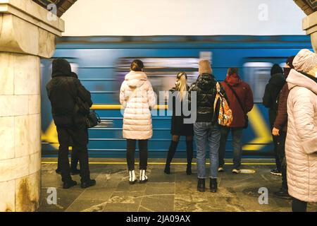 Menschen auf einer U-Bahn-Plattform auf dem Hintergrund einer vorbeifahrenden U-Bahn. Erwachsene Menschen auf U-Bahn-Plattform stehen, Zug in Bewegung. Stockfoto