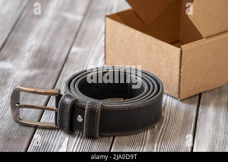 Stilvoller Gürtel aus schwarzem Leder und Stahlbeschlägen auf Holzhintergrund. Eine teure Geschenkoption für Männer, Frauen, hochwertiges Leder, ein schickes Surpris Stockfoto