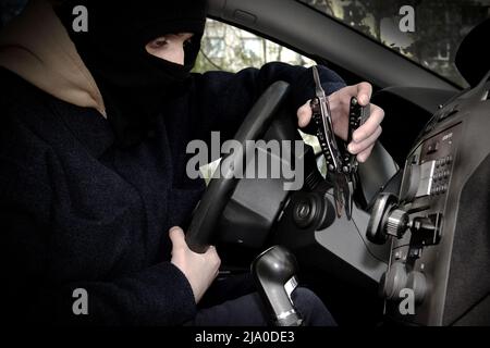 Ein Autodieb versucht, das Zündschloss mit einem Werkzeug zu öffnen. Der Autodieb versteckte sein Gesicht in einer Sturmhaube Stockfoto