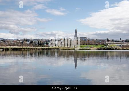 Reykjavik, Island, 25. April 2022: Die ikonische Hallgrimskirkja und ihre Umgebung spiegeln sich in einem kleinen See in der Nähe des Flughafens Vatmsmyri wider Stockfoto