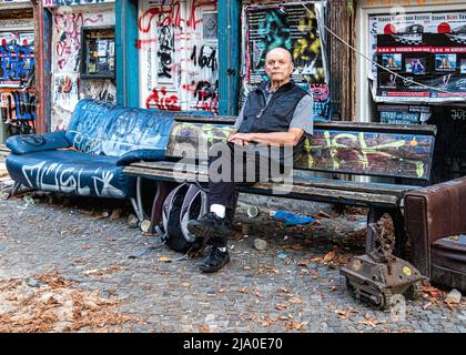 Berlin Kastanienallee 86, Senior Mann auf der Bank vor dem alten historischen Gebäude. Ein alternatives Wohnungsbauprojekt, das von Bewohnern gegen Gentrifizierung besetzt wird Stockfoto