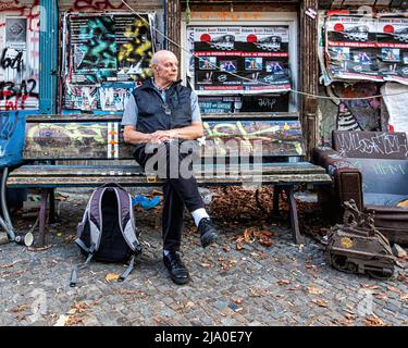 Berlin Kastanienallee 86, Senior Mann auf der Bank vor dem alten historischen Gebäude. Ein alternatives Wohnungsbauprojekt, das von Bewohnern gegen Gentrifizierung besetzt wird Stockfoto