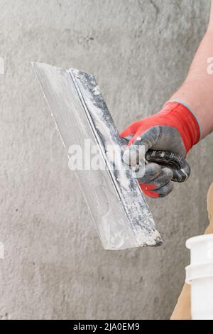 Breiter Spatel zum Nivellieren der Oberfläche von Wänden und Decken hält der Meister einen Spatel in der Hand. Stockfoto