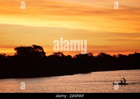 Silhouette von Fischern auf einem kleinen Holzboot auf dem Parana River in der Dämmerung, Esquina, Provinz Corrientes, Argentinien. Stockfoto