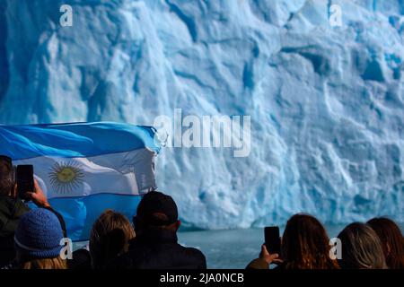 Touristen machen Fotos vom Spegazzini-Gletscher vom Boot aus, mit der argentinischen Flagge im Vordergrund, Los Glaciares-Nationalpark, Argentinien. Stockfoto