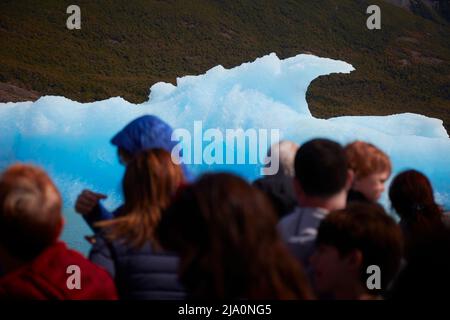 Touristen stehen vor einem blauen Eisberg während der Fahrt im Argentino See, Los Glaciares Nationalpark, Argentinien. Stockfoto