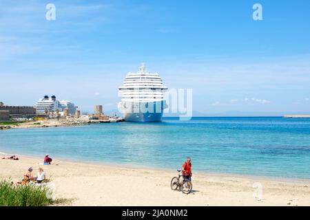 Blick über einen Strand auf das Costa Venezia-Schiff, das in der Mandraki Marina bei einem Besuch in Rhodos-Stadt, Rhodos, Griechenland, festgemacht wurde Stockfoto