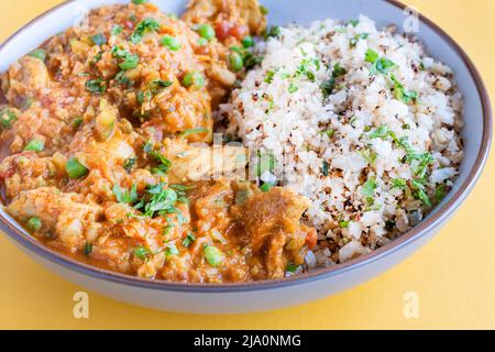 Ein hausgemachtes Chicken-Zucchini-Tikka-Masala-Kurvé, serviert in einer Schüssel mit Blumenkohlreis. Eine gesunde proteinreiche Mahlzeit, die keto freundlich ist Stockfoto