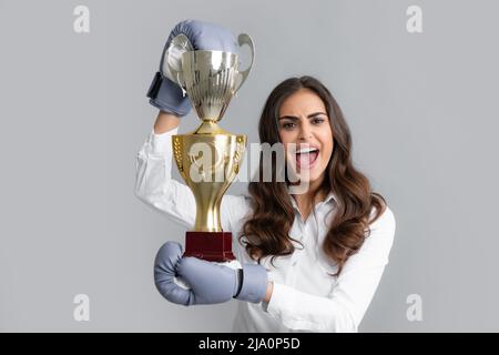 Frau in Boxhandschuhen halten Champion Siegerpokal, Trophäe. Schreiende starke junge Boxerin. Starke aggressive Geschäftsfrau Konzept. Gewinnerin weiblich Stockfoto