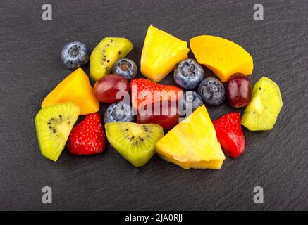Obstsalat mit Beeren und in Scheiben geschnittenen Früchten auf einer Steinoberfläche. Nahaufnahme. Stockfoto