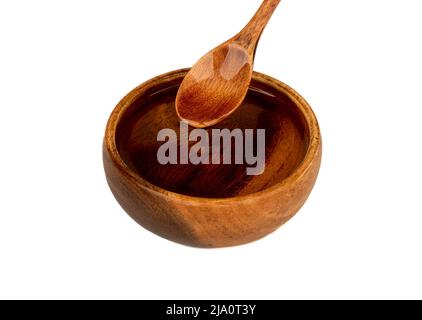 Sonnenblumenöl fließt von einem Holzlöffel in eine Holzschale. Kopierbereich, weißer Hintergrund. Stockfoto