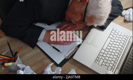 Müde schläfrig überarbeiteter älterer einschlafender Geschäftsmann sitzt mit Laptop am Schreibtisch des Heims Stockfoto