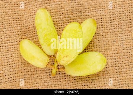 Mehrere Beeren weißer, kernloser Trauben auf Jutegewebe, Nahaufnahme, Draufsicht. Stockfoto