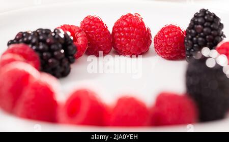 Himbeeren und Brombeeren auf einem weißen Teller im Kreis gelegt Stockfoto