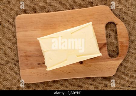 Ein Stück köstliche Butter auf einem Holzschneidebrett auf einem Jutetuch, Nahaufnahme, Draufsicht. Stockfoto