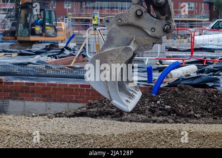 Bagger Nivellierung Schotter auf neue Wohnbau-Baustelle vor unfertigen Haus und Vermessungsgeräte Stockfoto