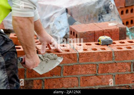 Maurerwerk, das Ziegelsteine auf Mörtel auf dem neuen Wohnhausbau verlegt Stockfoto