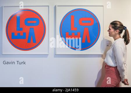 London, Großbritannien. 26.. Mai 2022. Ein Mitarbeiter von mannigfaltigen Editions posiert mit Gavin Turks 'Revolving Love (Orange)' und 'Revolving Love (Blue)'. Die London Original Print Fair 37. wird bis zum 29.. Mai 2022 im Somerset House eröffnet. Sie ist die am längsten laufende Druckmesse der Welt und wurde 1985 an der Royal Academy of Arts gegründet. Quelle: Imageplotter/Alamy Live News Stockfoto