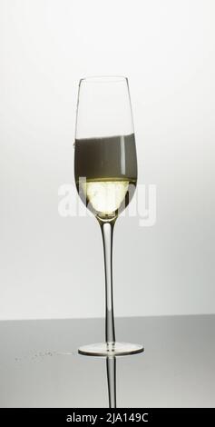 Vertikales Bild einer offenen Flasche, die Champagner in ein Tulpenglas auf weißem Hintergrund gießt Stockfoto