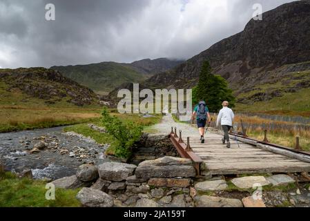 Paar wandern auf dem Watkin-Pfad, Snowdonia Nationalpark. Überquerung der Brücke durch Plascwmllan und neben der Afon Cwm Llan. Stockfoto