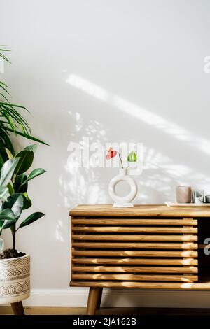 Moderne Einrichtung im minimalistischen skandinavischen Stil. Nordische Keramikvase mit roter Anthuriumblume, Kerzen auf einer Holzkonsole. Grünhaus Pflanzen in Töpfen Stockfoto