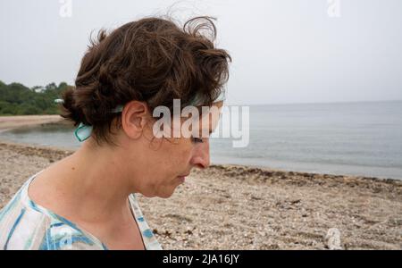 Lage Schoß einer Frau mittleren Alters mit braunem Haar am Strand auf einem coludy Tag im Sommer. Casual active leisue Umweltkonzept Bild. Stockfoto