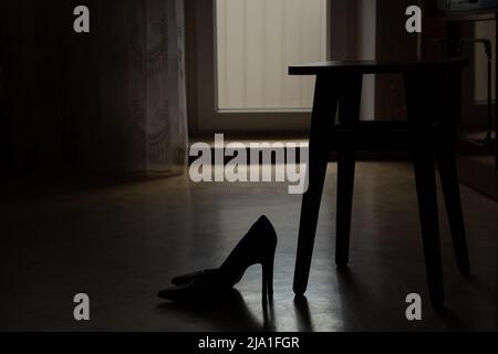 Frauen-Schuhe mit hohen Absätzen stehen auf dem Boden des Hauses in der Nähe eines Holzstuhls im Dunkeln, modische Damenschuhe, Schuhe mit Absätzen Stockfoto